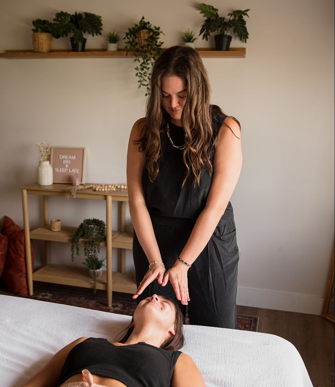 Heather Flynn holding her hands over a client resting on a healing table in a calm, plant-filled studio